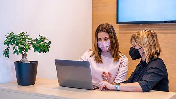 Female Dentist and patient wearing protective face mask discussing over laptop in clinic