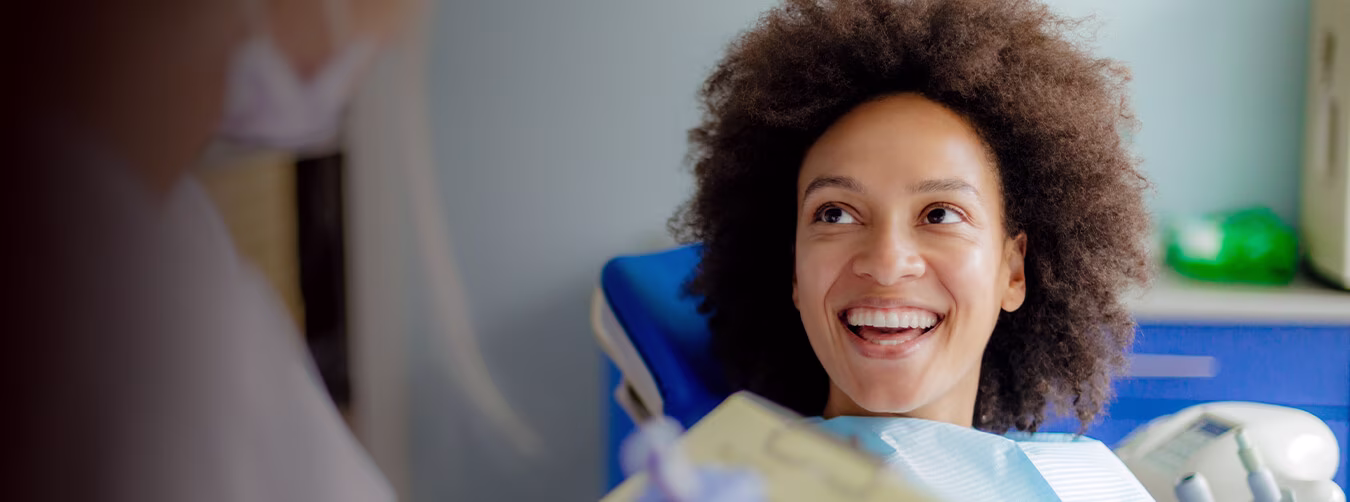 A smiling patient is sitting on a dental chair while looking at the hygienist