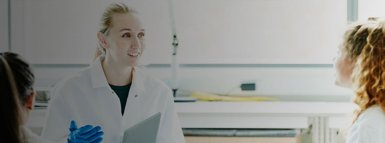 a scientist with a lab white lab coat, blue gloves, and folder speaking in front of a group of people